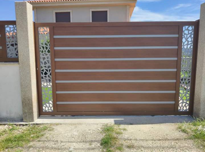 Portão em ferro com painéis castanhos e trabalho decorativo de corte laser nos laterais